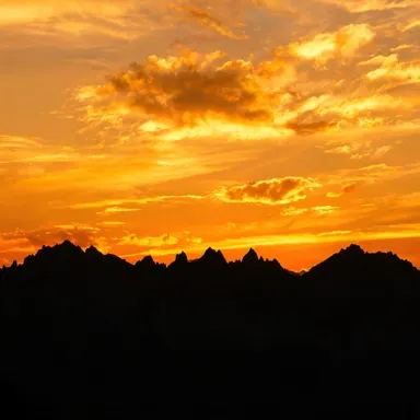 A breathtaking sunset over a mountain range, warm golden and orange hues painting the sky, silhouetted peaks, dramatic clouds