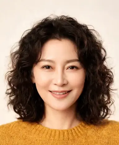Studio portrait of a friendly woman in her 30s with curly dark hair, warm smile, mustard sweater, soft neutral backdrop, faci