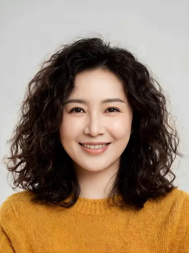 Studio portrait of a friendly woman in her 30s with curly dark hair, warm smile, mustard sweater, soft neutral backdrop, faci