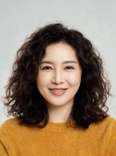 Studio portrait of a friendly woman in her 30s with curly dark hair, warm smile, mustard sweater, soft neutral backdrop, faci