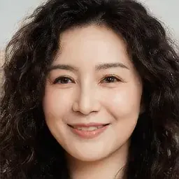Studio portrait of a friendly woman in her 30s with curly dark hair, warm smile, mustard sweater, soft neutral backdrop, faci