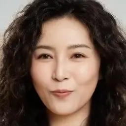 Studio portrait of a friendly woman in her 30s with curly dark hair, warm smile, mustard sweater, soft neutral backdrop, faci