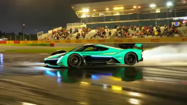 Electric Formula E car sliding broadside through a flooded night circuit hairpin, camera whip-panning to follow the drift, am