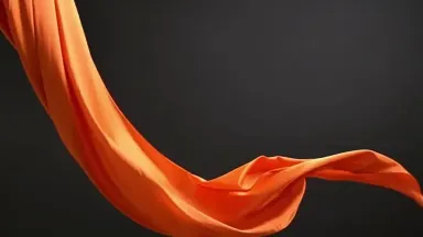 A ribbon of orange silk unfurling in slow motion against deep charcoal, studio light catching the folds, premium abstract com