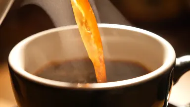 A ceramic cup of coffee being poured in extreme slow motion, warm backlight through the steam, premium advertising macro