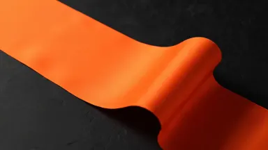 A ribbon of orange silk unfurling in slow motion against deep charcoal, studio light catching the folds, premium abstract com
