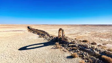 Orbit the surviving arch clockwise at a steady altitude, the long shadow rotating slowly beneath it across the cracked earth 