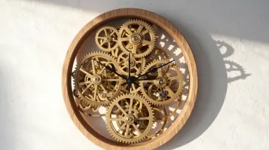 Camera tilts slowly downward from the clock face to the lowest visible gear cluster while the brass gears turn at their natur