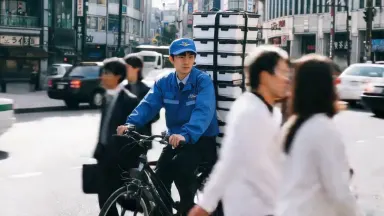 The deliveryman pushes off and weaves forward through traffic as pedestrians flow past on either side. Camera orbits counterc