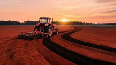 Whip pan rapidly from left to right across the plowed furrows to the tractor cab and engine stack, the motion blur of red cla