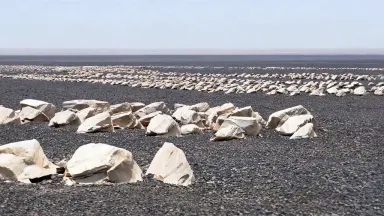Camera holds completely still as a slow rack focus shifts from the sharp foreground ventifacts to the row of stones at mid-di