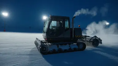 Snowcat operator navigating a slope-grooming machine across an empty piste at midnight under stadium lights, tracking shot ru