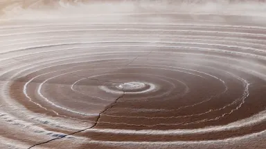 Desiccated Atacama lake bed at noon, concentric rings of white mineral salt and deep rust expanding outward from a cracked ce