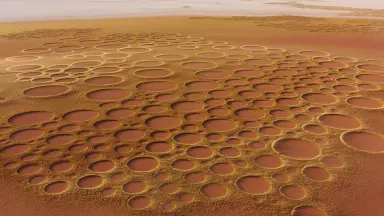Aerial view locked off static above Namibian red grassland at golden hour, hundreds of bare fairy circles spaced in a near-pe
