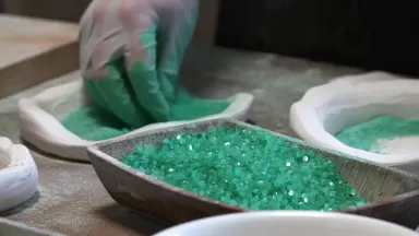 Pâte de verre artist packing crushed glass powder into an open plaster mold on a workbench, whip pan sweeping from a bowl of 