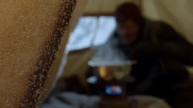 Static frame inside a canvas base camp mess tent, rack focus pulling from a foreground frost-dusted tent wall to an expeditio