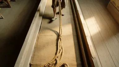 Rope maker walking backward down a long ropewalk twisting three hemp strands into a single hawser, the braid tightening in re