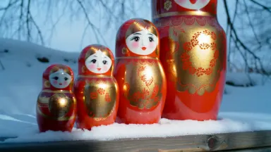 Intricately painted ceramic matryoshka dolls arranged in descending size across a snow-covered outdoor bench, camera beginnin