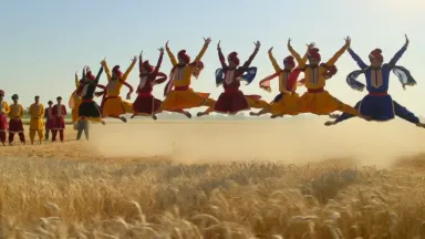 Bhangra dancers in vibrant embroidered kurtas and turbans leaping in synchronized arcs above a golden Punjabi wheat field at 