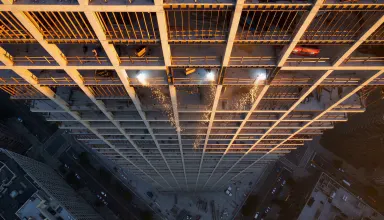Exposed structural steel skeleton of a half-built high-rise at sunrise, welders sparks falling forty floors above street leve