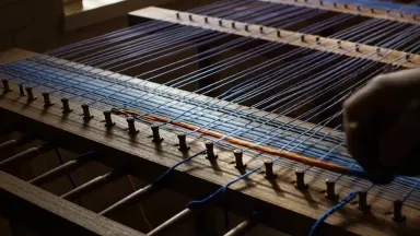 Warp threads being wound in a chevron pattern onto a warping board in a dim dyehouse, tracking shot alongside the moving hand