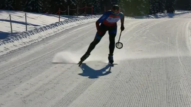 A cross-country skate-skier in a racing suit executes a powerful V2 stride across a wide sunlit groomed plateau, poles planti
