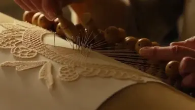 A lacemaker's hands work rapidly over a cylindrical pillow crowded with bobbins, crossing and pinning punto de Venezia thread