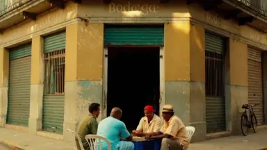 A group of men play dominoes on overturned plastic crates outside a Havana corner bodega, slapping tiles down, laughing and g