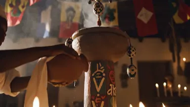 Voodoo ceremony in a candlelit Haitian peristyle, a mambo in white cloth pouring libation from a clay vessel onto a richly de