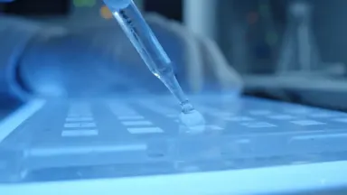 Gene sequencing technician loading a DNA fragment into an electrophoresis gel tray, slow dolly out from extreme close on a pi