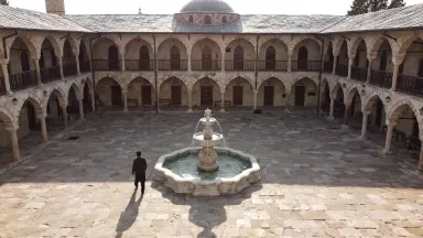 Ottoman hans caravanserai courtyard shot top down overhead, carved marble fountain at center sending a thin stream of water r