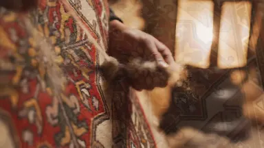 Rugmaker hand-knotting a Tibetan pile rug on a vertical frame, fingers tying a single ghiordes knot with practiced precision,