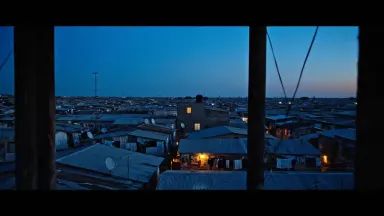 Slow push in from a water tower platform over a dense corrugated iron shantytown roofscape at blue hour, the camera drifting 