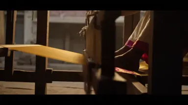 Photoreal. A vivid silk sari being woven on a pit loom in a narrow Varanasi workshop sunk below street level, a weaver's feet